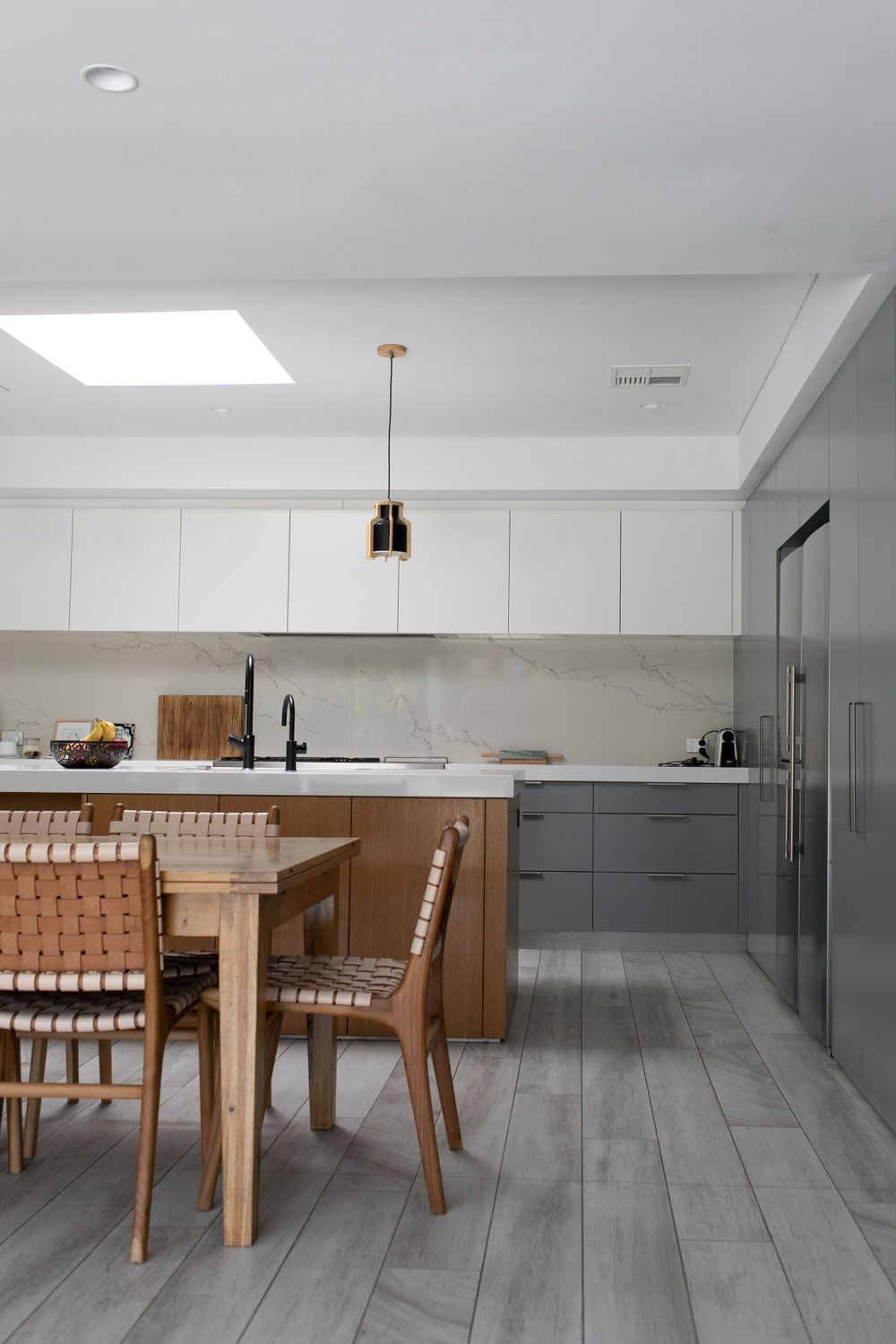 Modern kitchen with timber dining chairs, marble splashback, and skylight above.