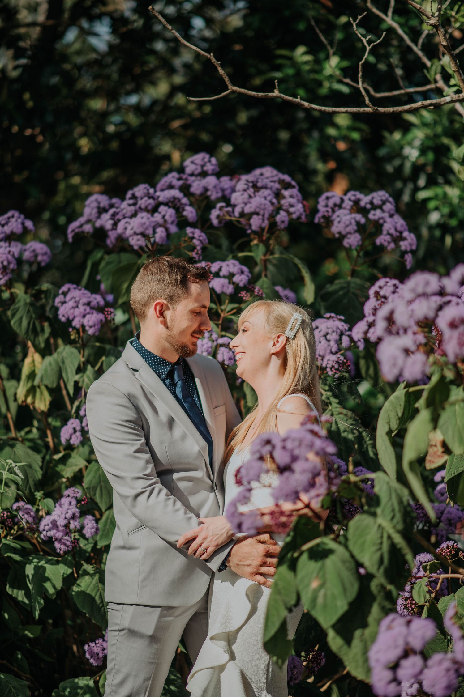 Couple shares tender moment among blooming purple hydrangeas in garden setting.