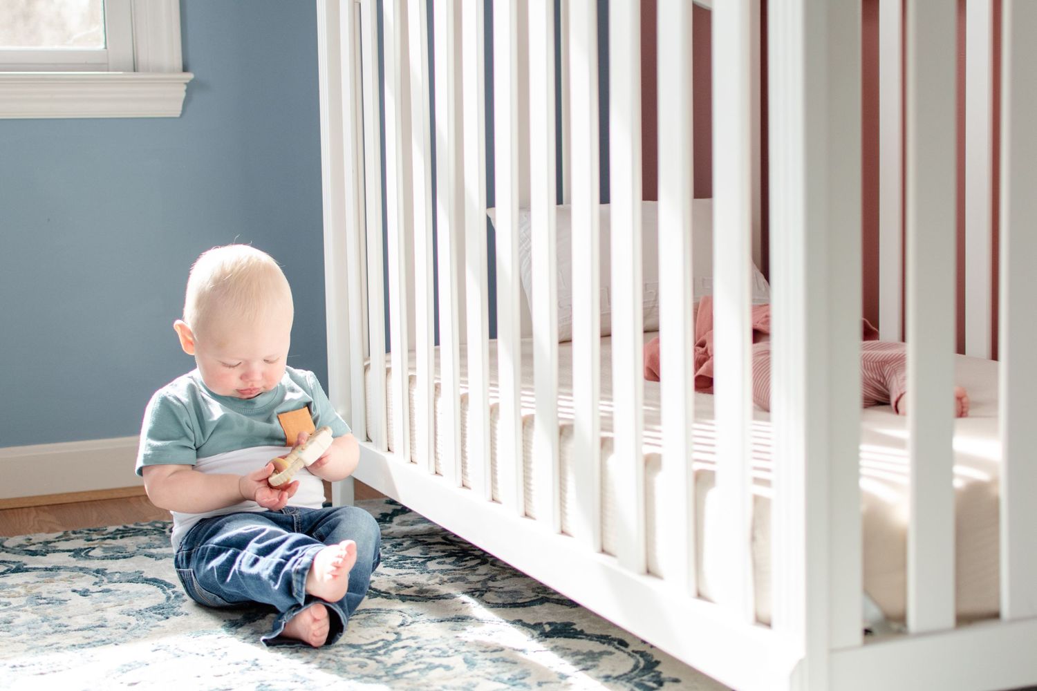Young child sitting on floor by white railing holding a toy.