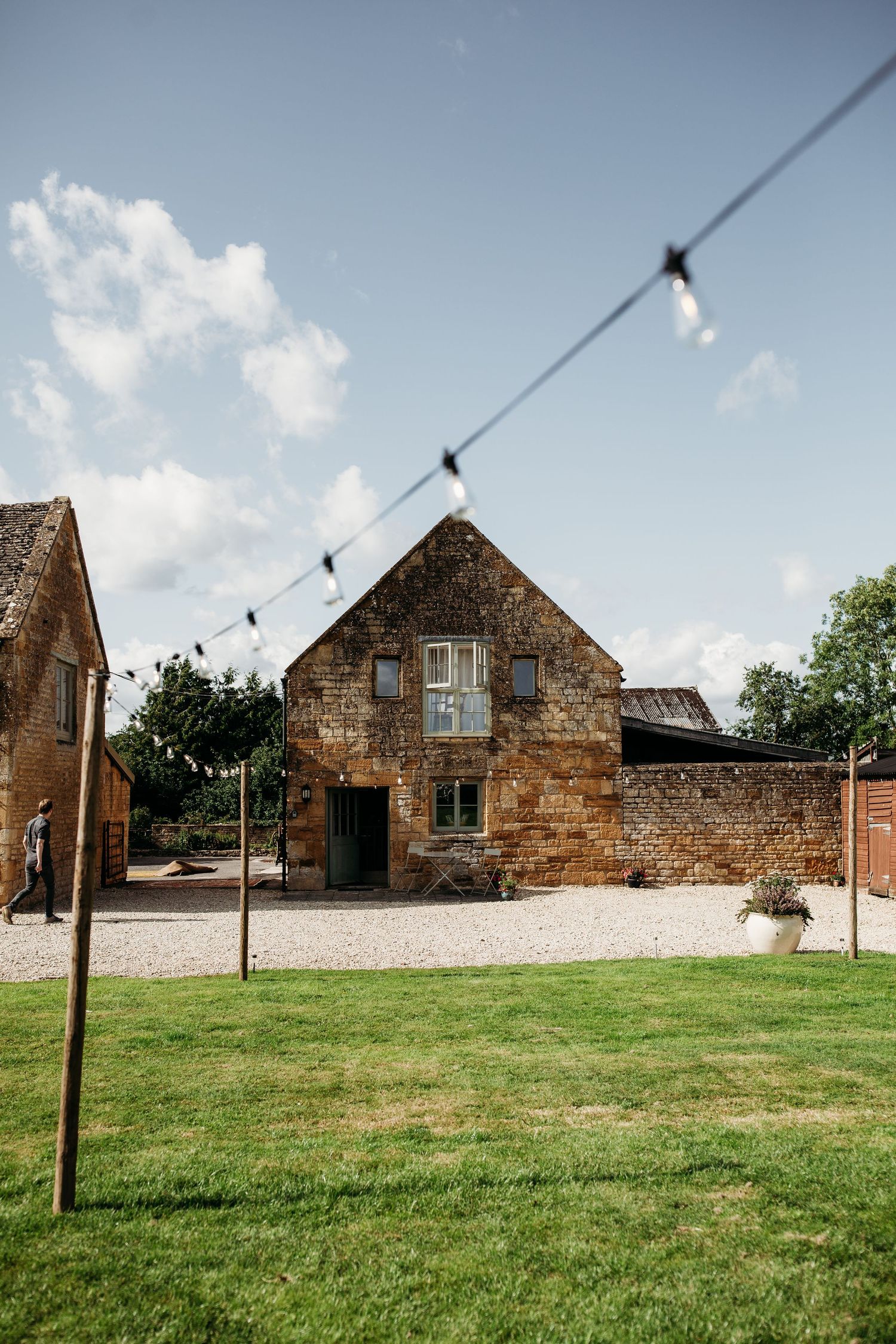 A charming stone barn venue with string lights and a grassy lawn on a sunny day.