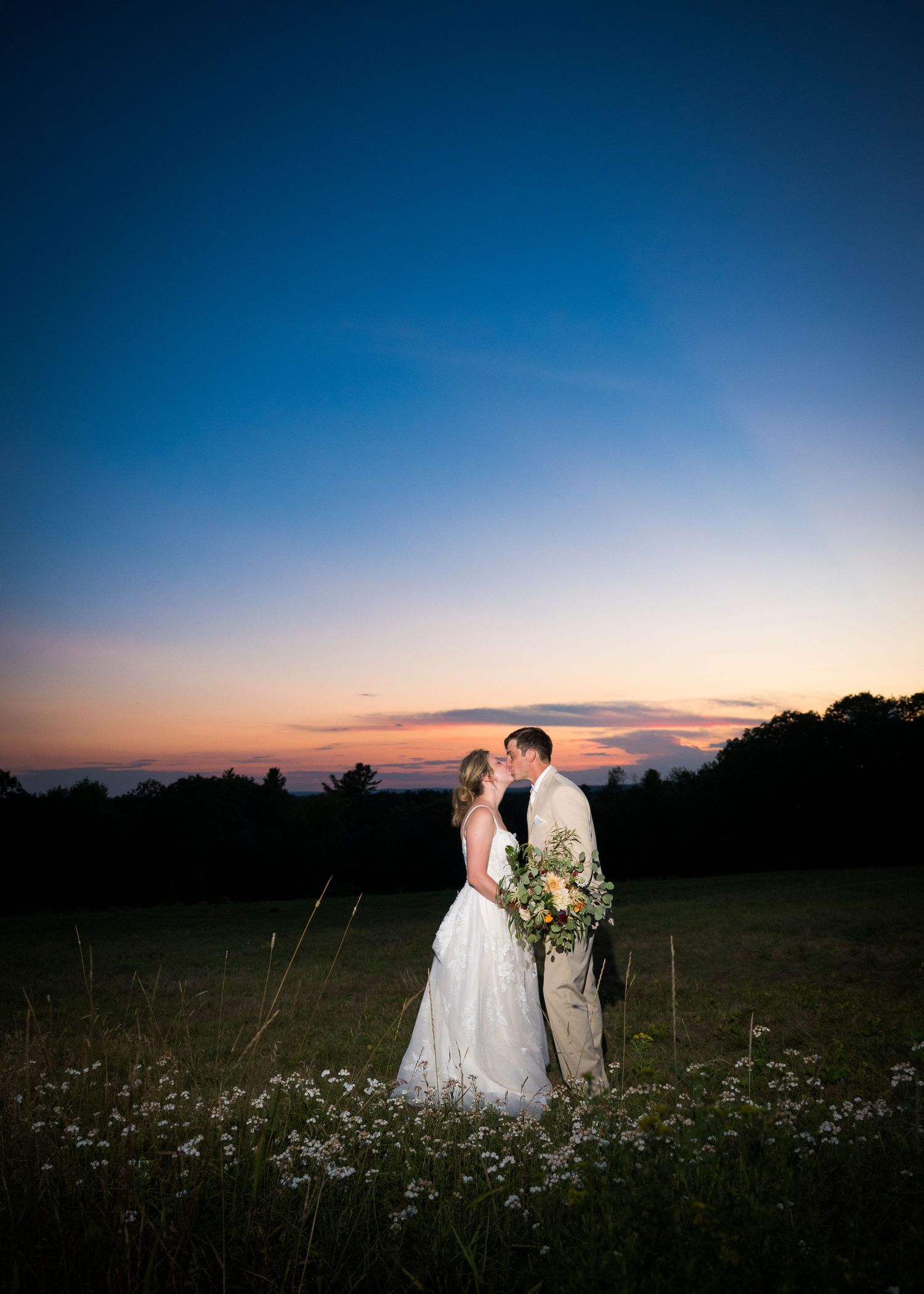 A couple embraces during sunset in a wildflower meadow with dramatic sky backdrop.