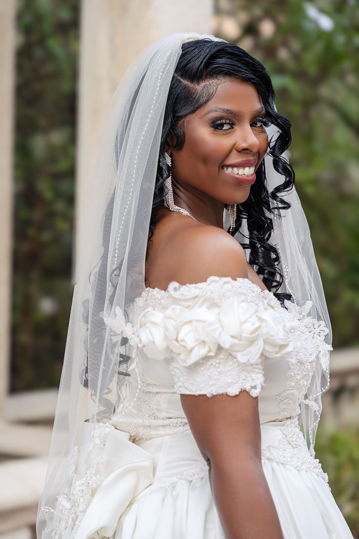 Beautiful bride wearing off-shoulder white gown and long veil smiles during wedding portraits.
