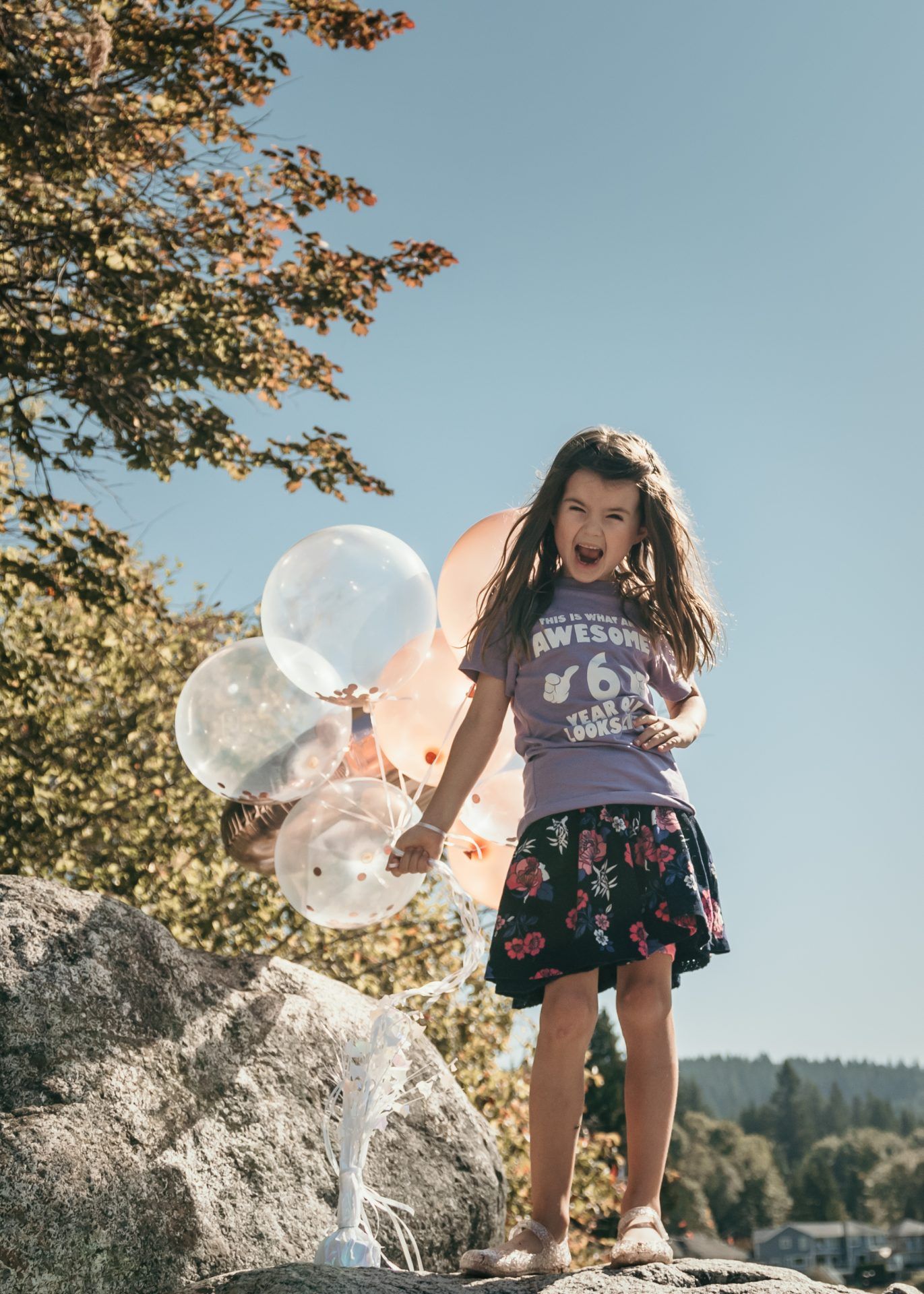 Playful outdoor portrait with translucent balloons against an autumn tree backdrop.
