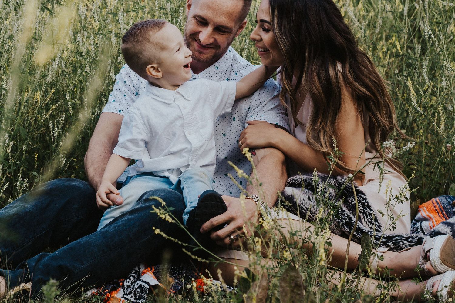 Laughing family sits in a field while son touches mother's face