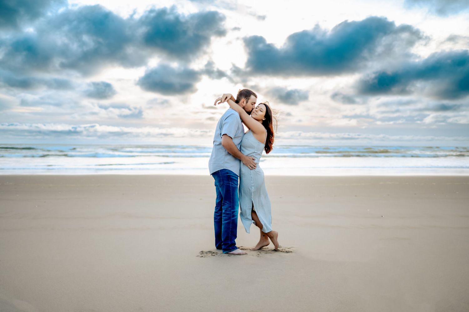 Dramatic beach photography session with cloudy skies and ocean waves.