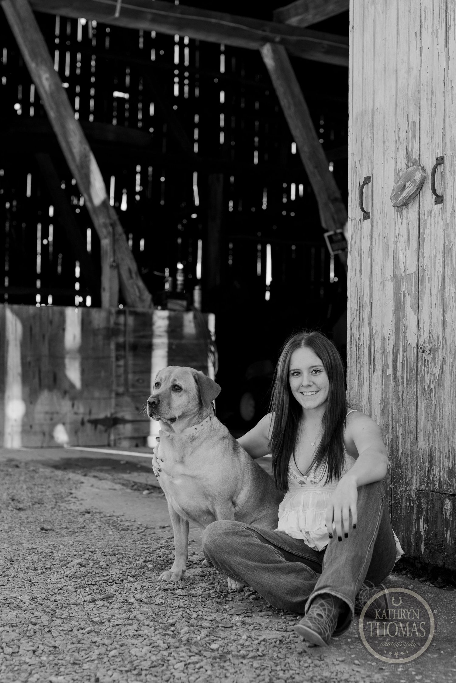 Black and white portrait with friendly dog inside rustic barn setting.