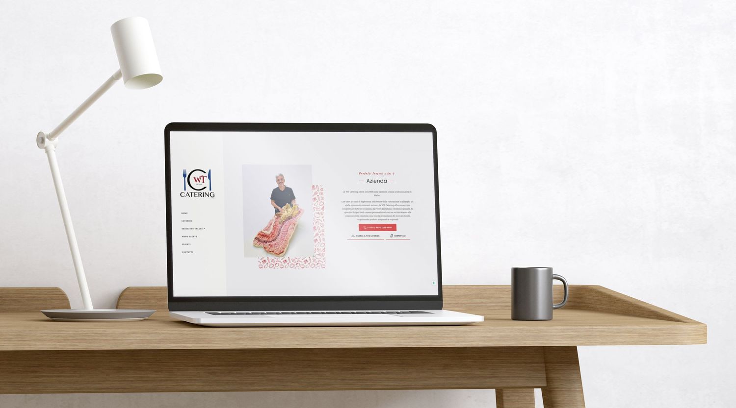 A minimalist desk setup with a laptop displaying a website, desk lamp, and coffee mug on wooden surface.