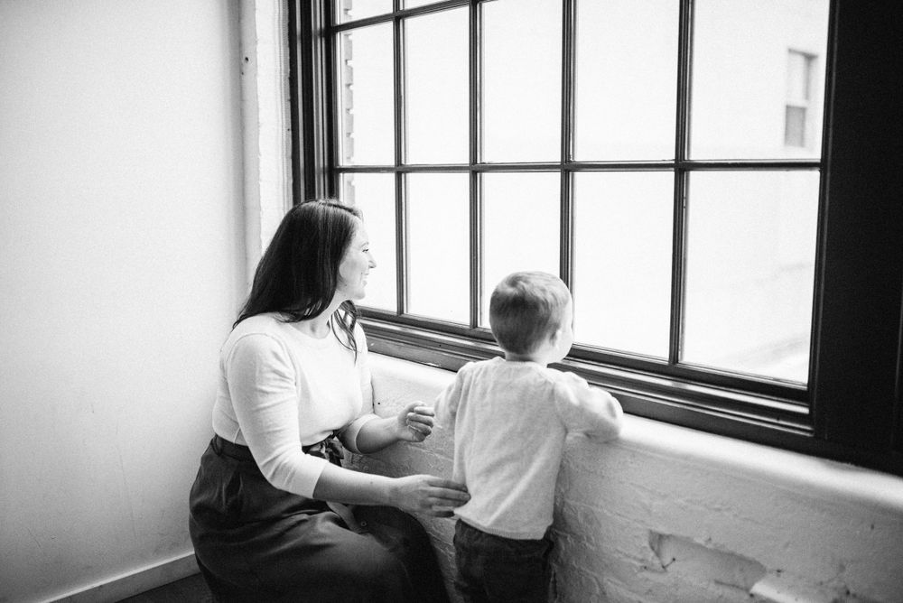 Black and white photo of parent and child gazing out bright window together.