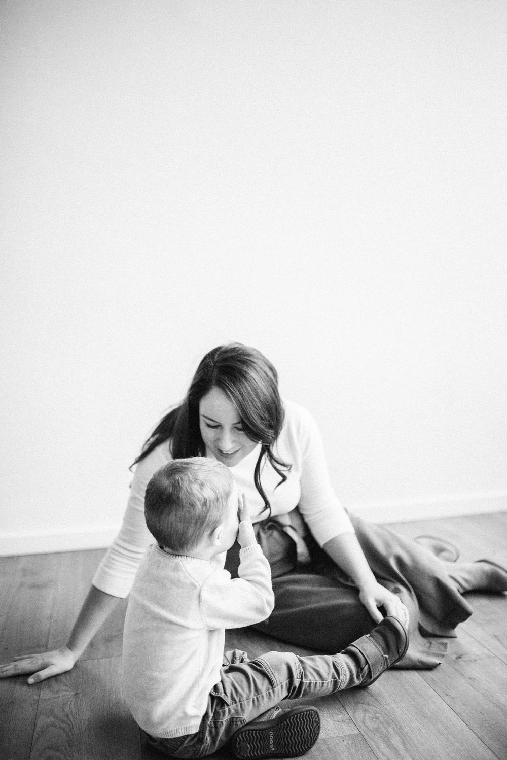 Black and white indoor portrait of parent and child sitting together on wooden floor.