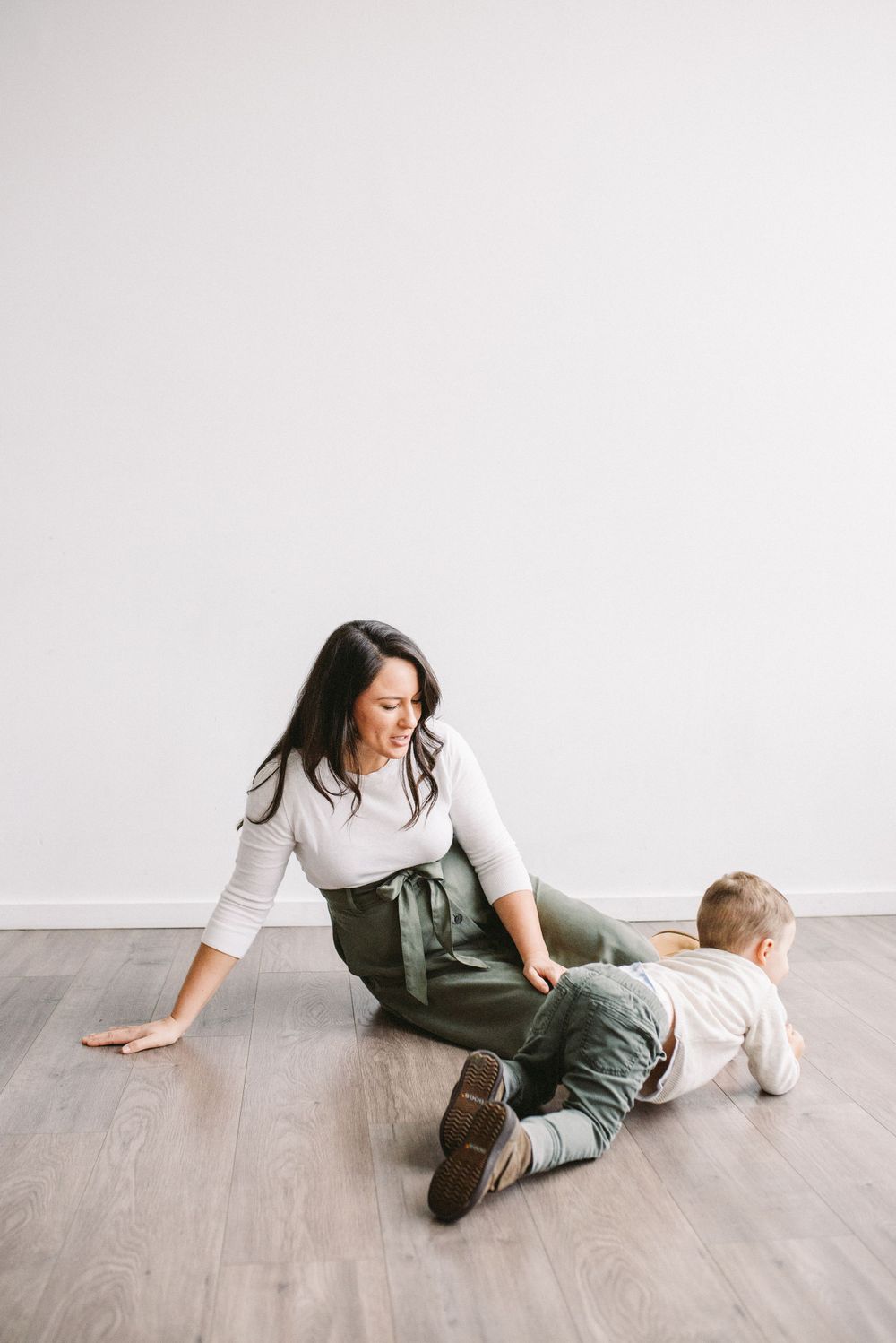 Playful scene of adult and child lying on wooden floor in casual attire.