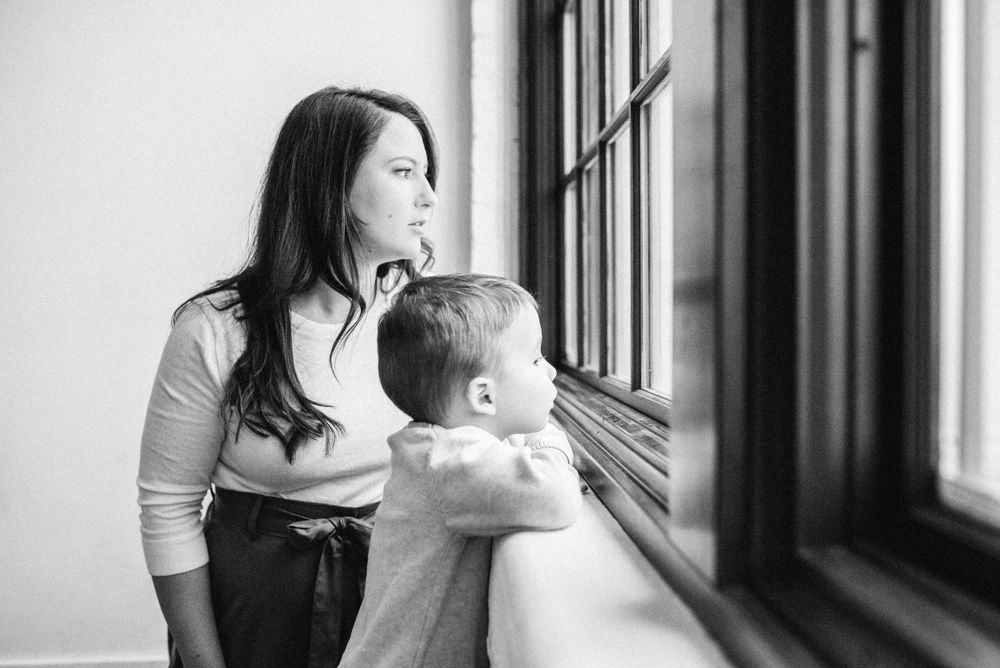 Parent and child looking out window together in black and white indoor portrait.