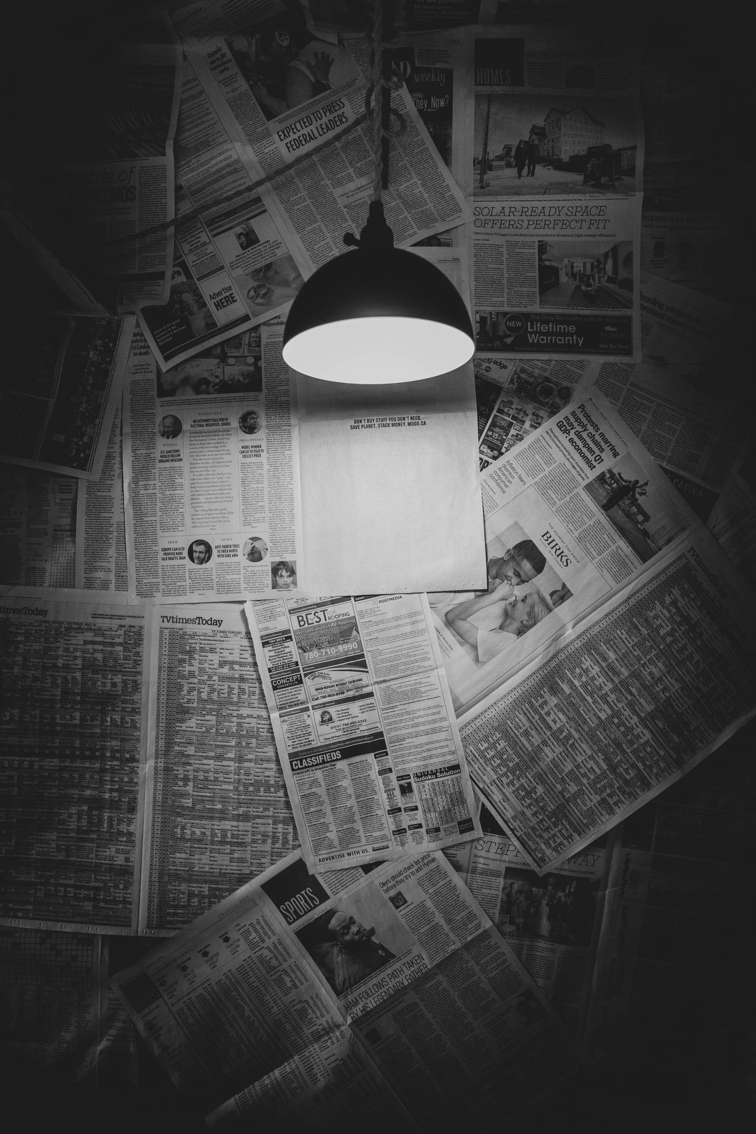 A hanging lamp illuminates scattered newspaper pages in moody black and white.
