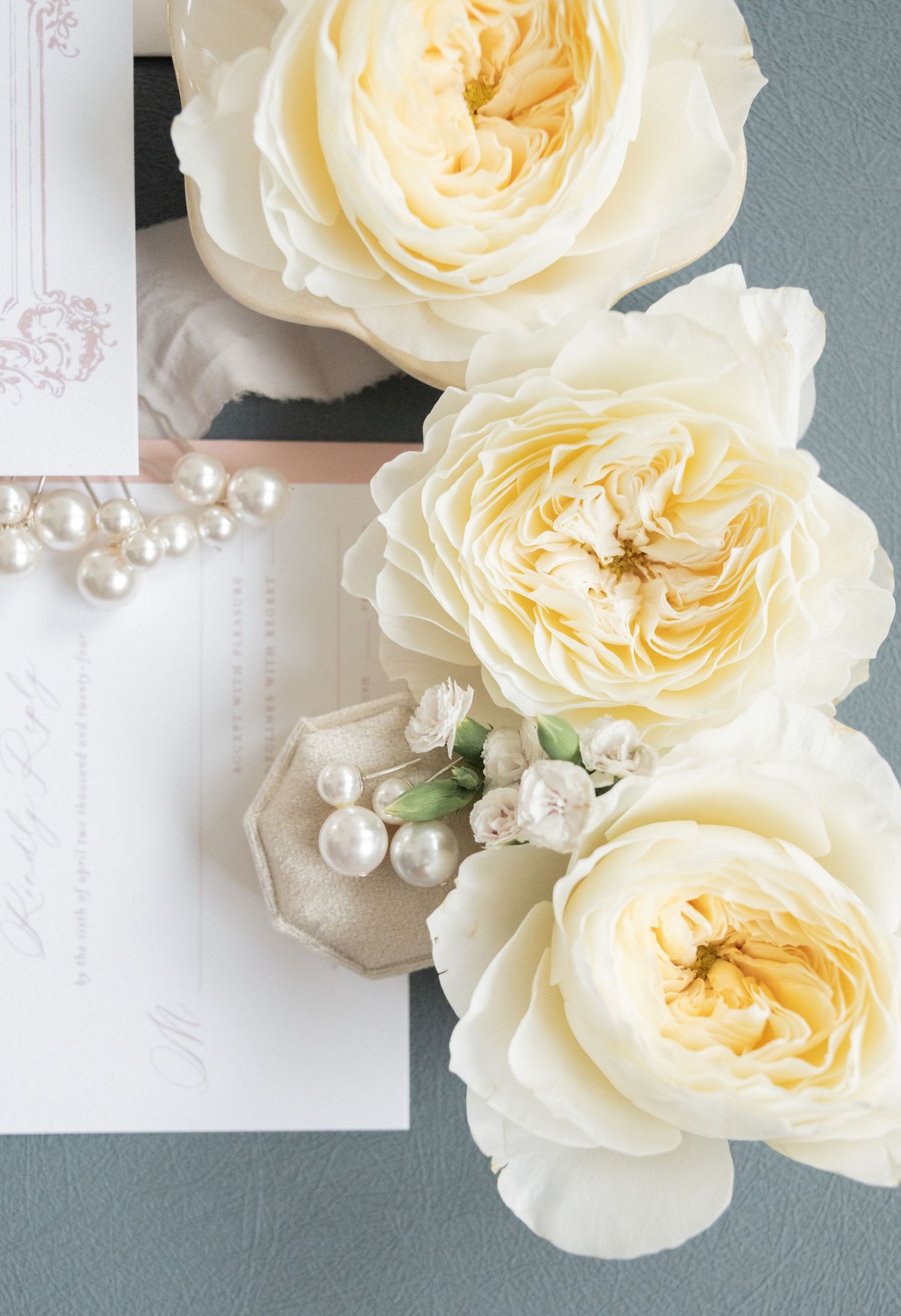 Soft cream garden roses with scattered pearls against white stationery.