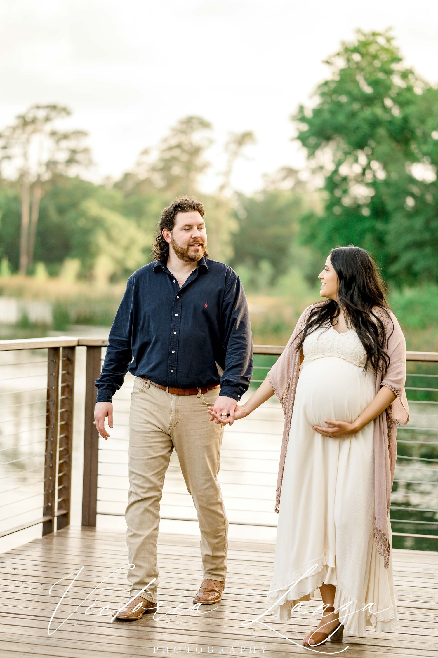 Couple strolling on wooden boardwalk during sunset engagement session.