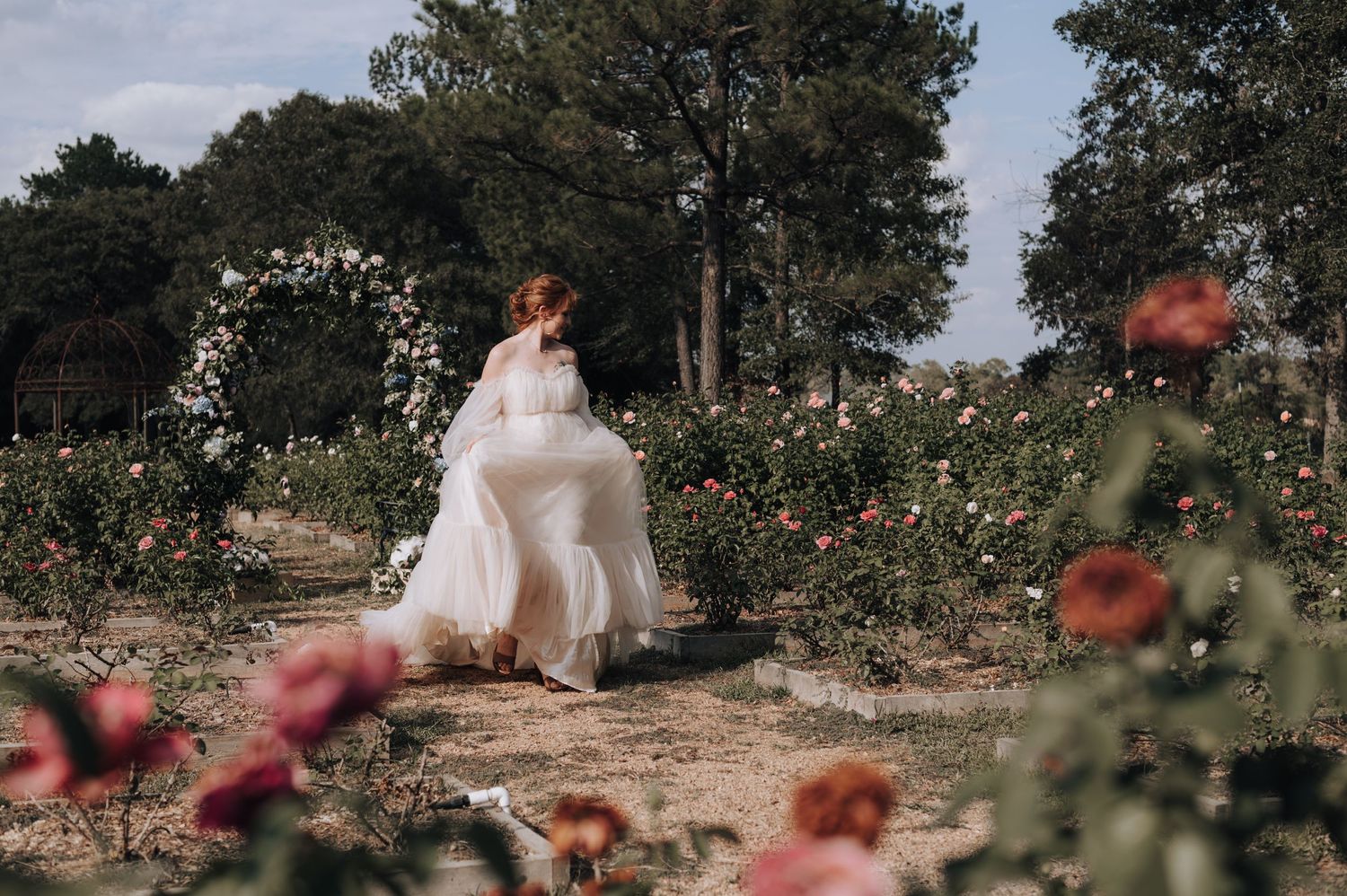 Flowing white wedding gown captured in motion among roses and a garden arch.