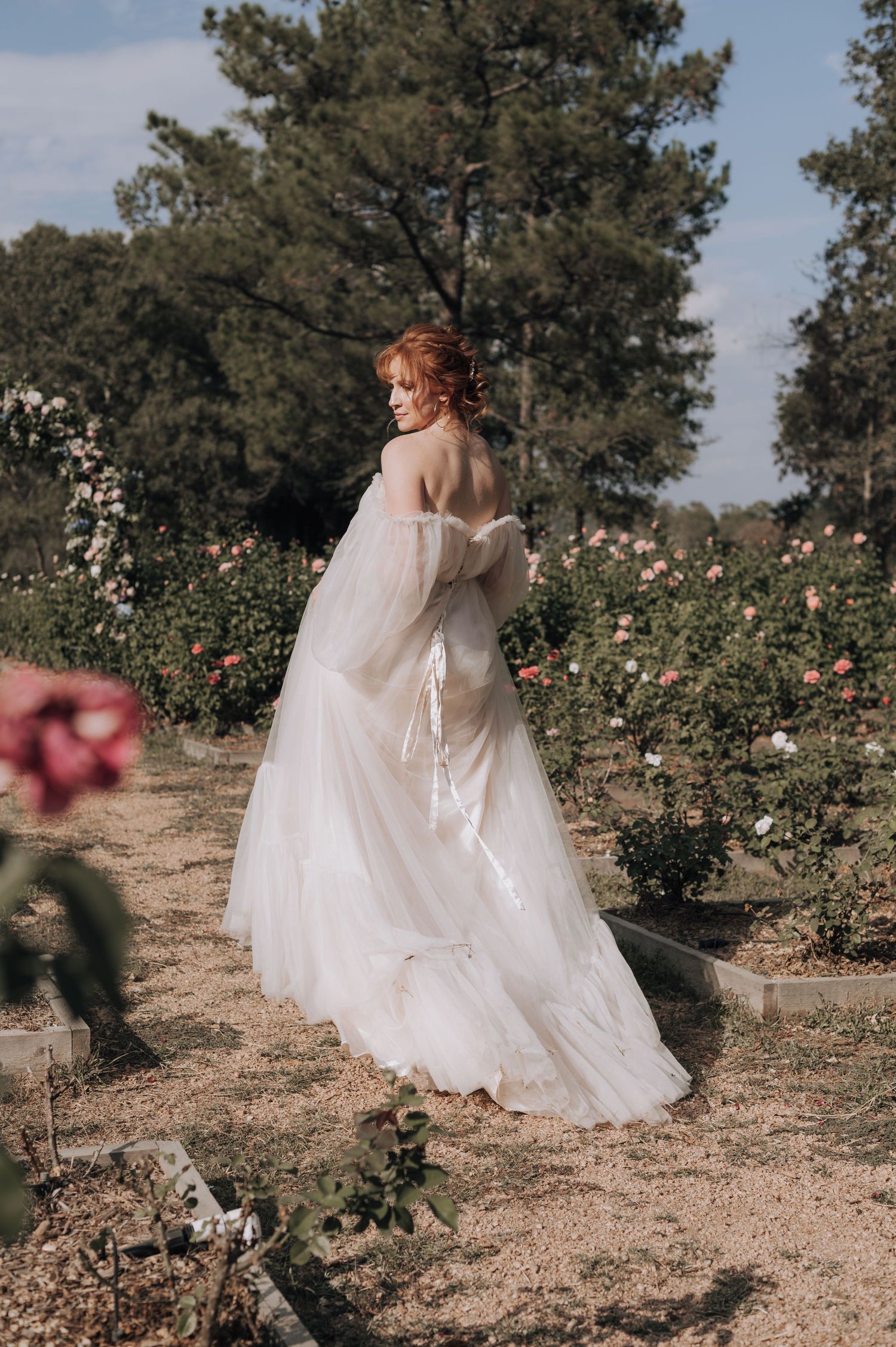 Elegant off-shoulder wedding dress photographed in a blooming rose garden.