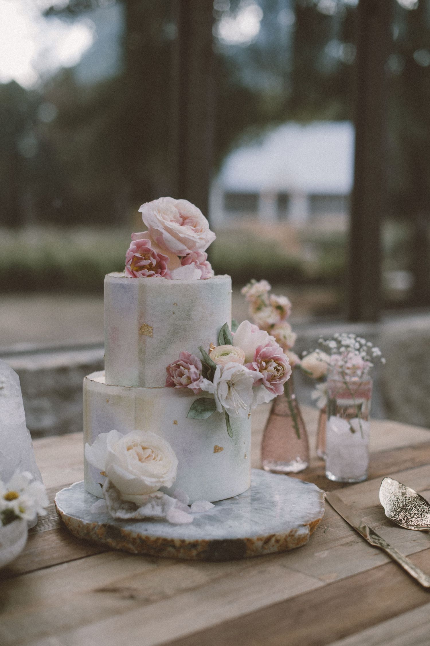 Elegant two-tier white wedding cake decorated with fresh pink roses on wooden table.