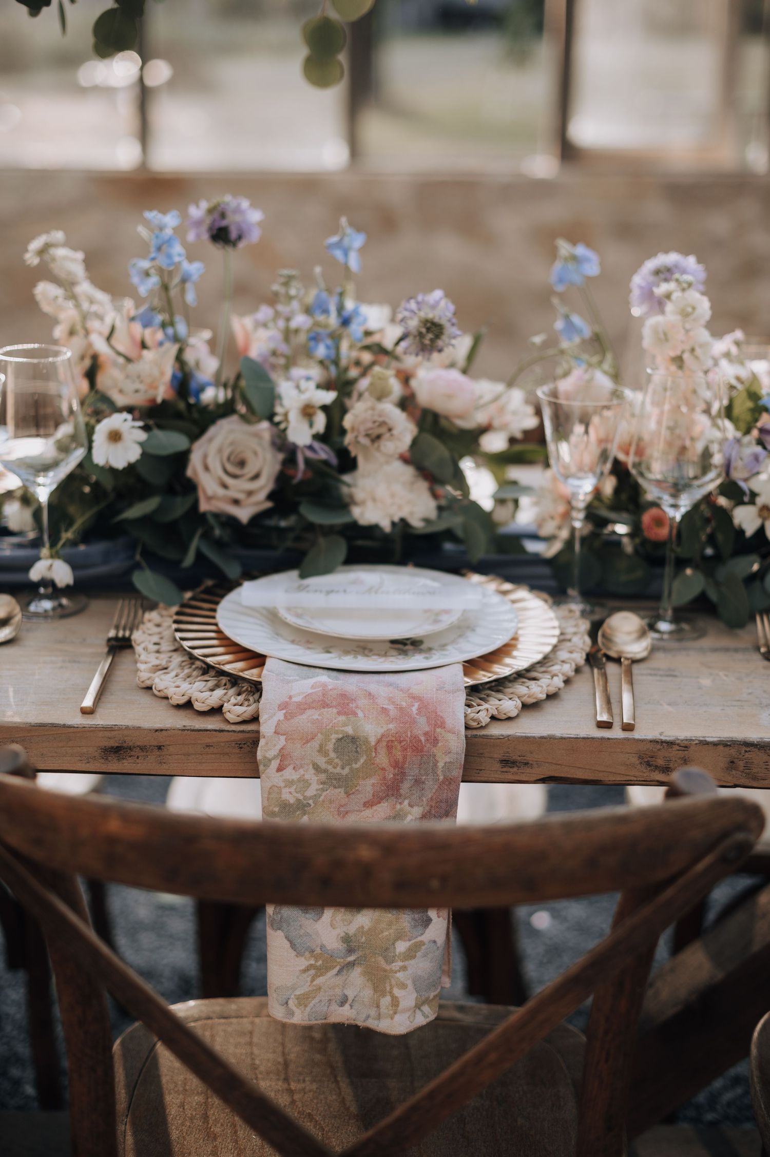 Intimate place setting with floral centerpiece featuring roses and delicate blue flowers on rustic wooden table.