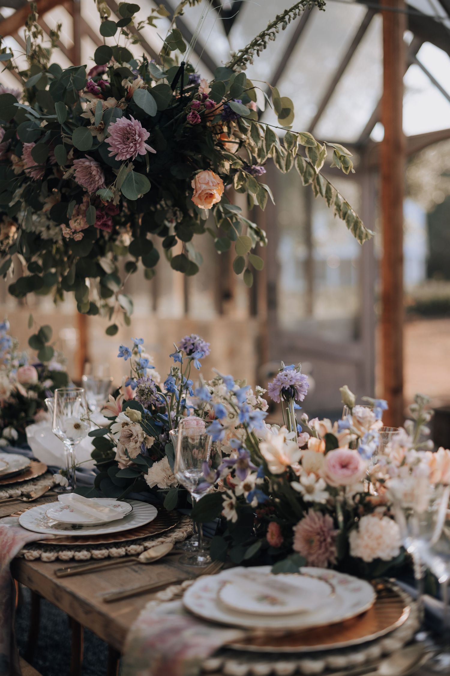Romantic table setting with pink and purple floral arrangements, crystal glassware, and vintage place settings.