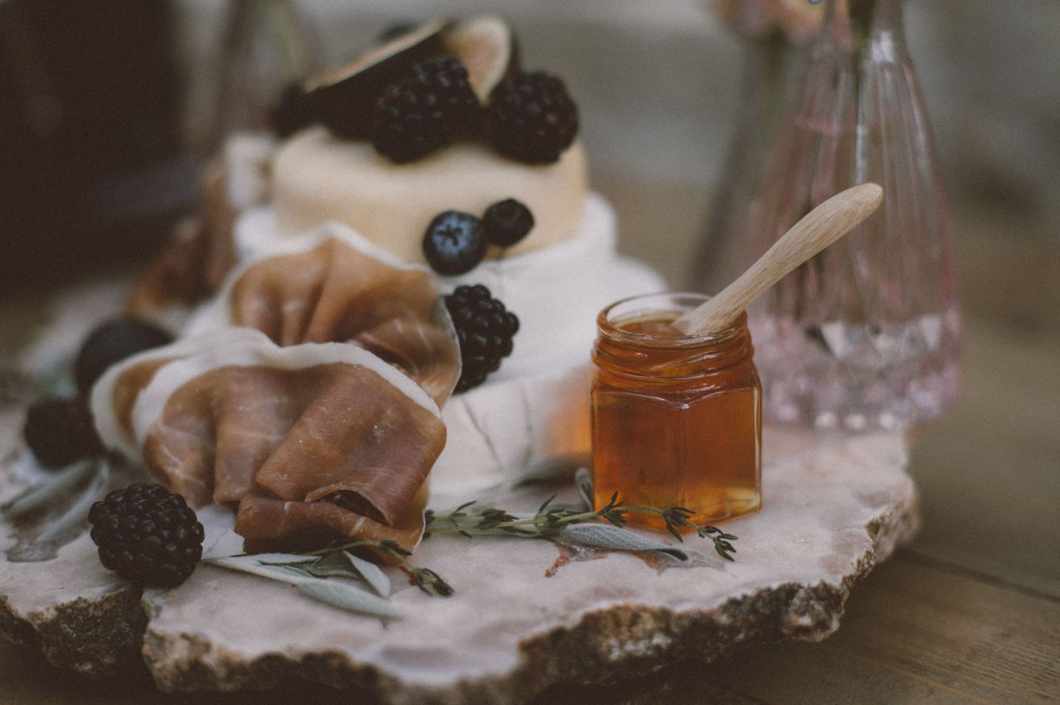 Rustic dessert plate with blackberries, honey, and pastries on white surface.