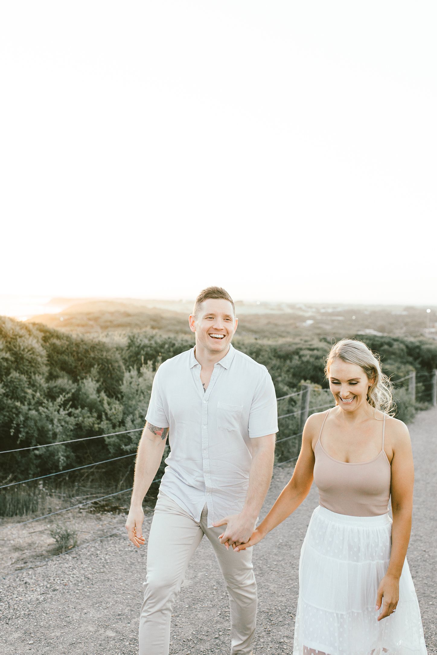 Happy couple holding hands while walking along a hilltop trail during sunset.