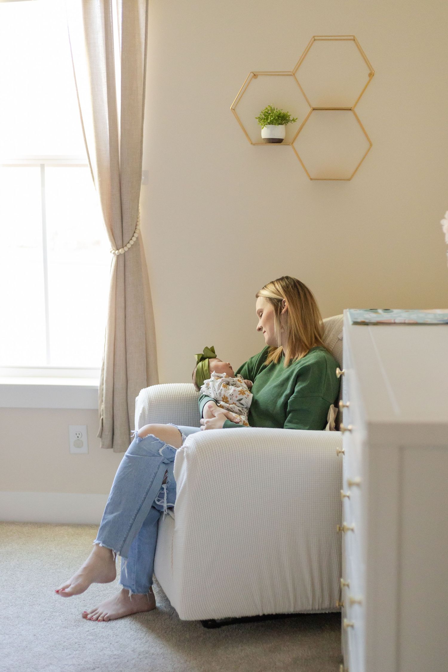 A woman sits in a white chair near hexagonal wall shelves in a bright room.