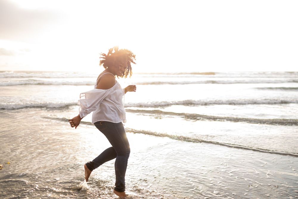 Silhouette of person dancing joyfully on beach at sunset.
