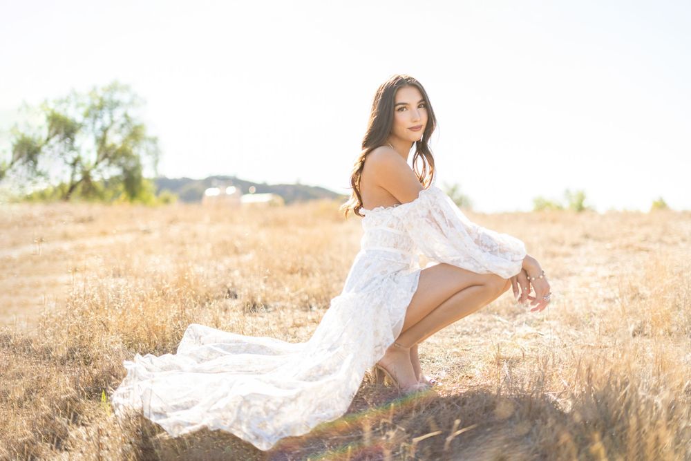 A person in a flowing white dress poses dramatically in a golden wheat field at sunset.