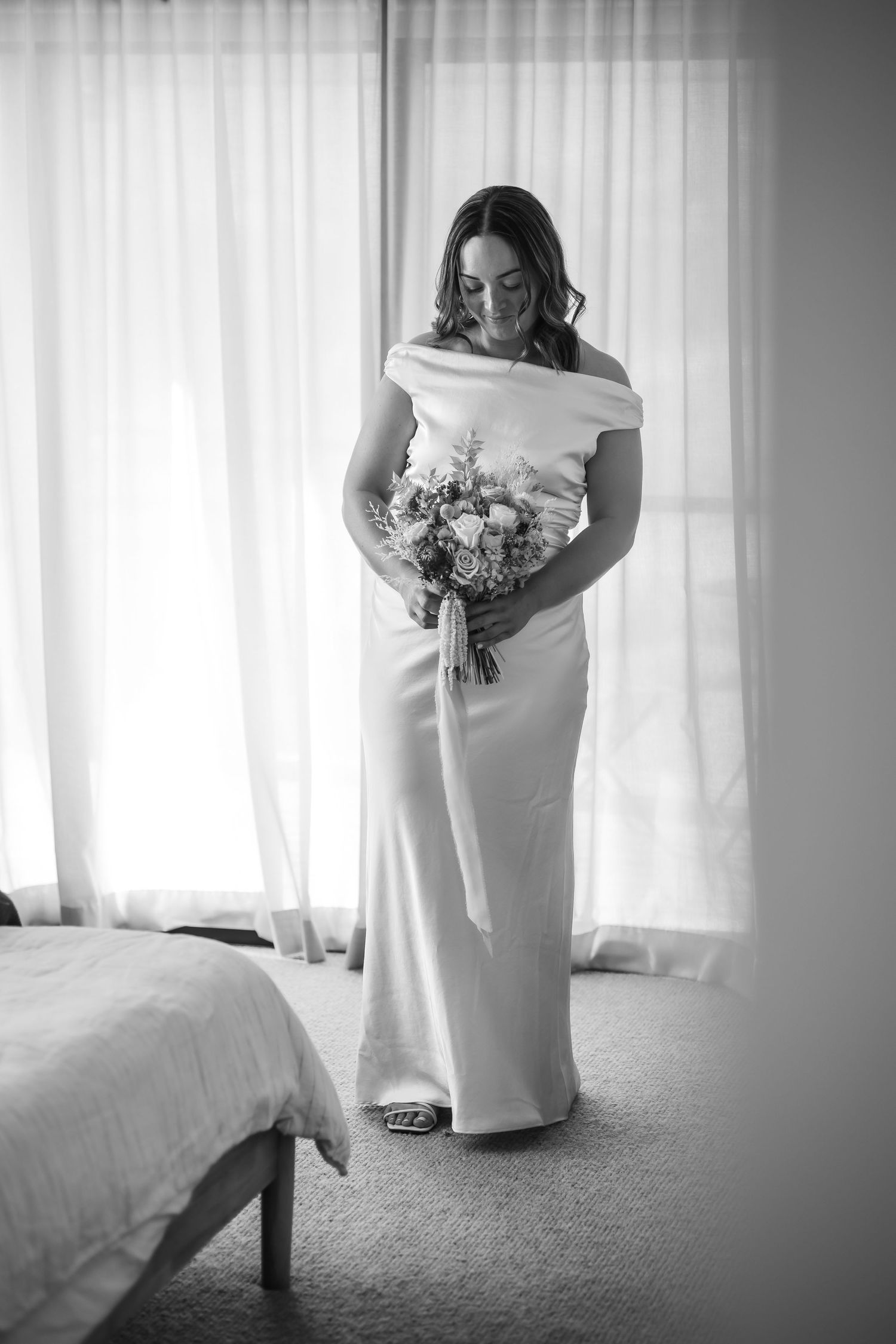 Black and white portrait of wedding dress details near window with soft lighting.