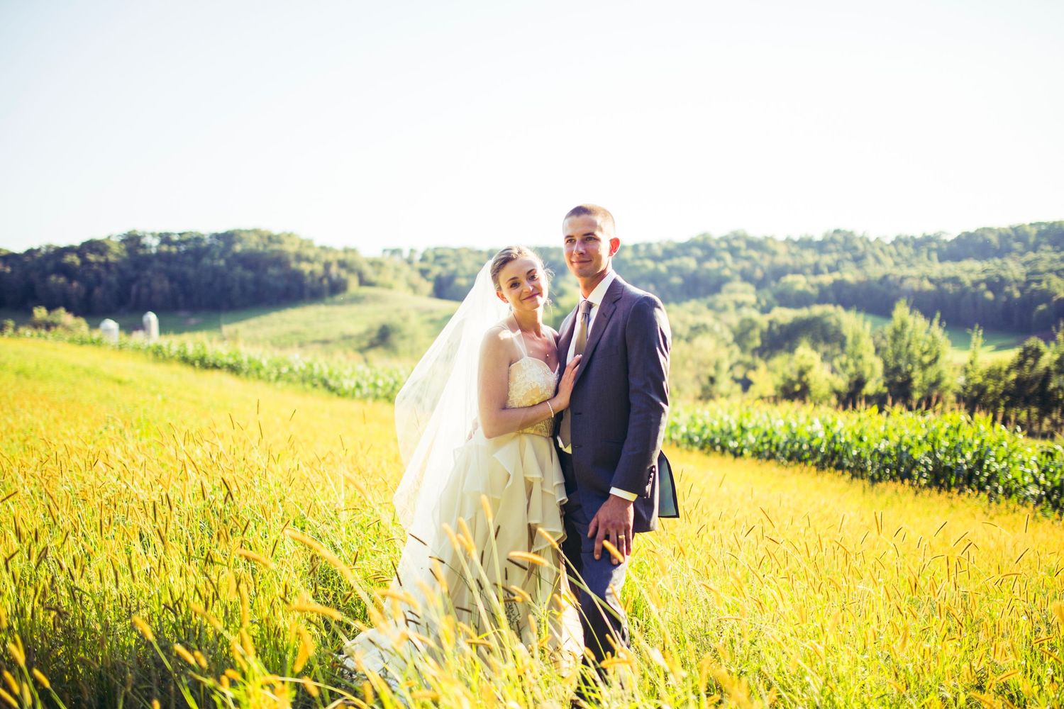 A couple poses together in a golden wheat field during sunset for romantic wedding photos.
