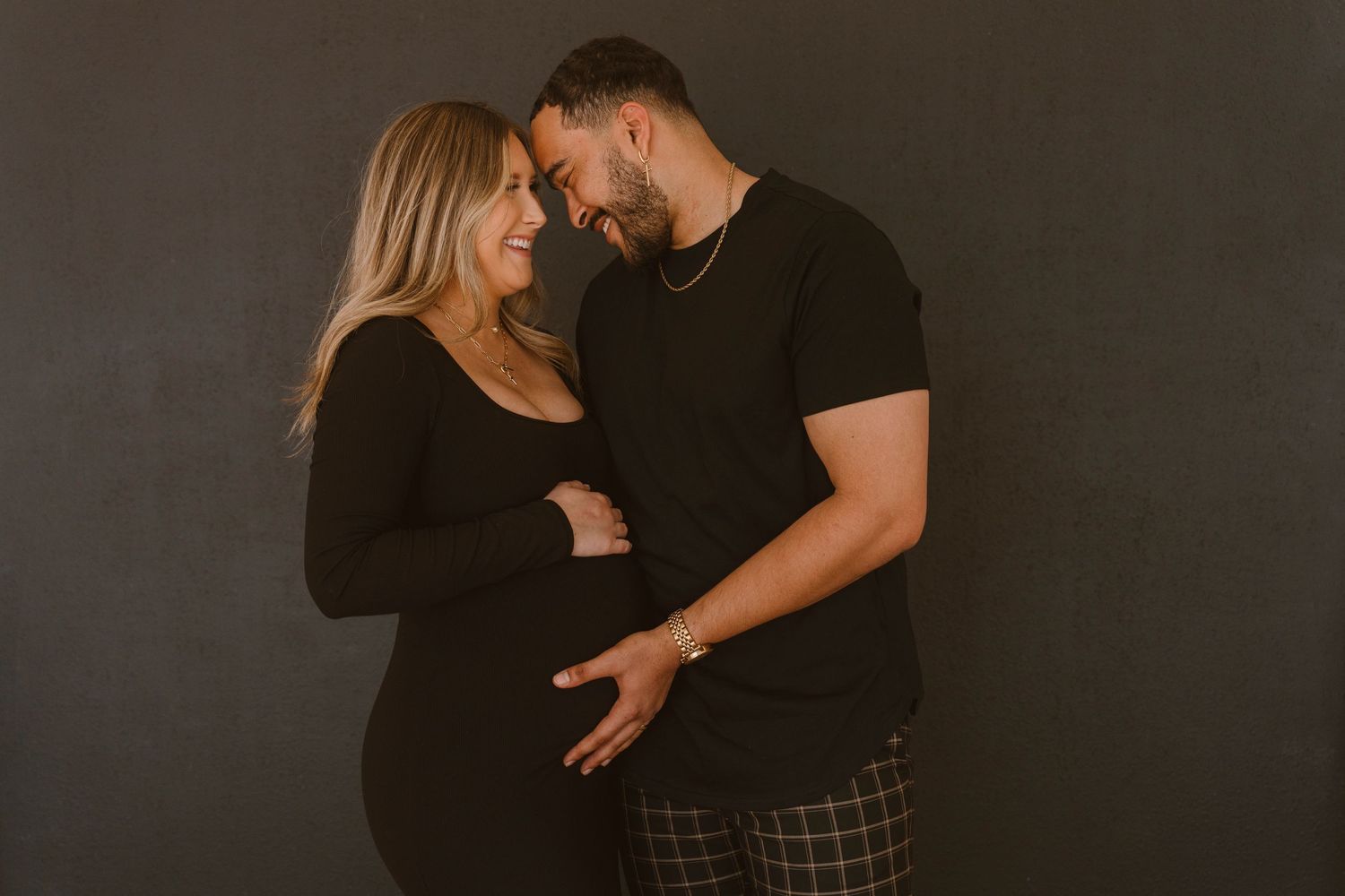 Studio maternity photography session in Plano Texas. Couple embracing each other smiling holding pregnant belly.