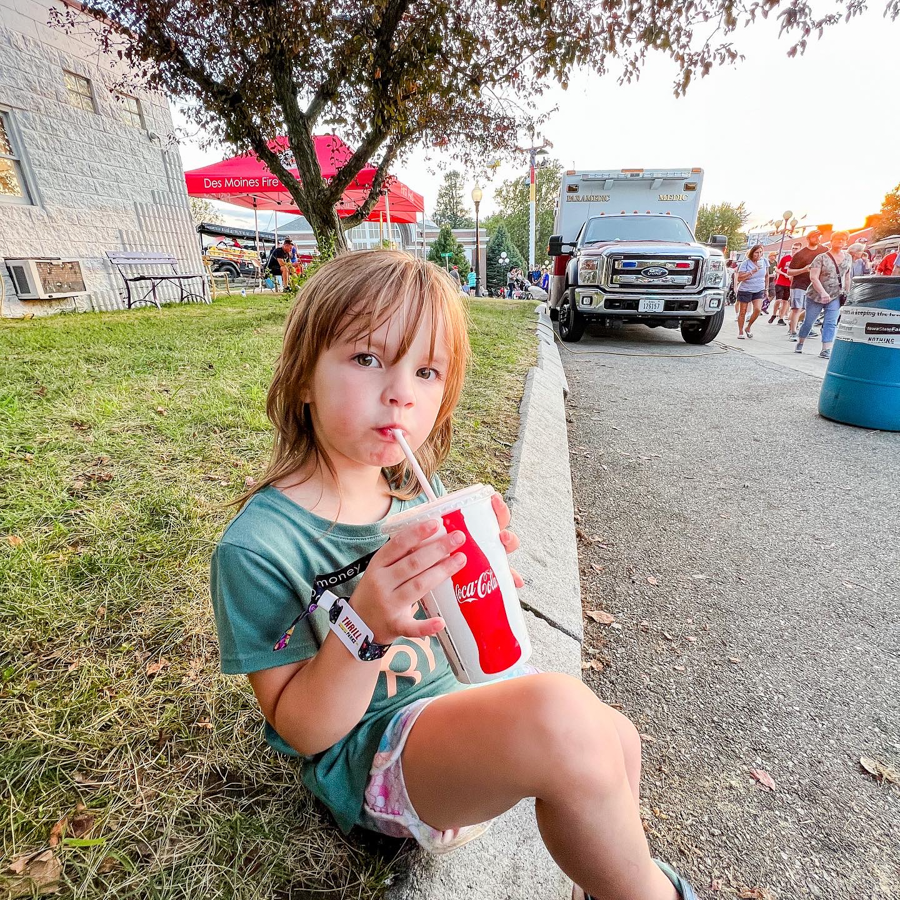 Person enjoying a beverage while sitting near a tree at an outdoor event.