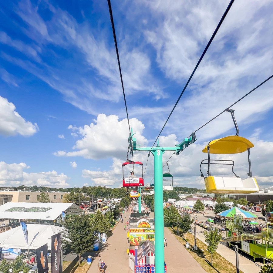Colorful ski lift chairs against bright blue sky overlooking a fairground.