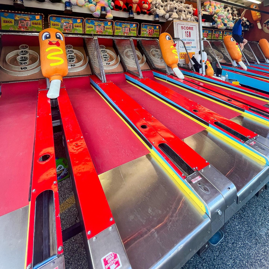 Colorful carnival game with hot dog shaped targets on red and rainbow striped lanes.