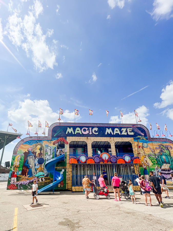 Colorful Magic Maze carnival attraction with festive flags and waiting crowd at a fairground.