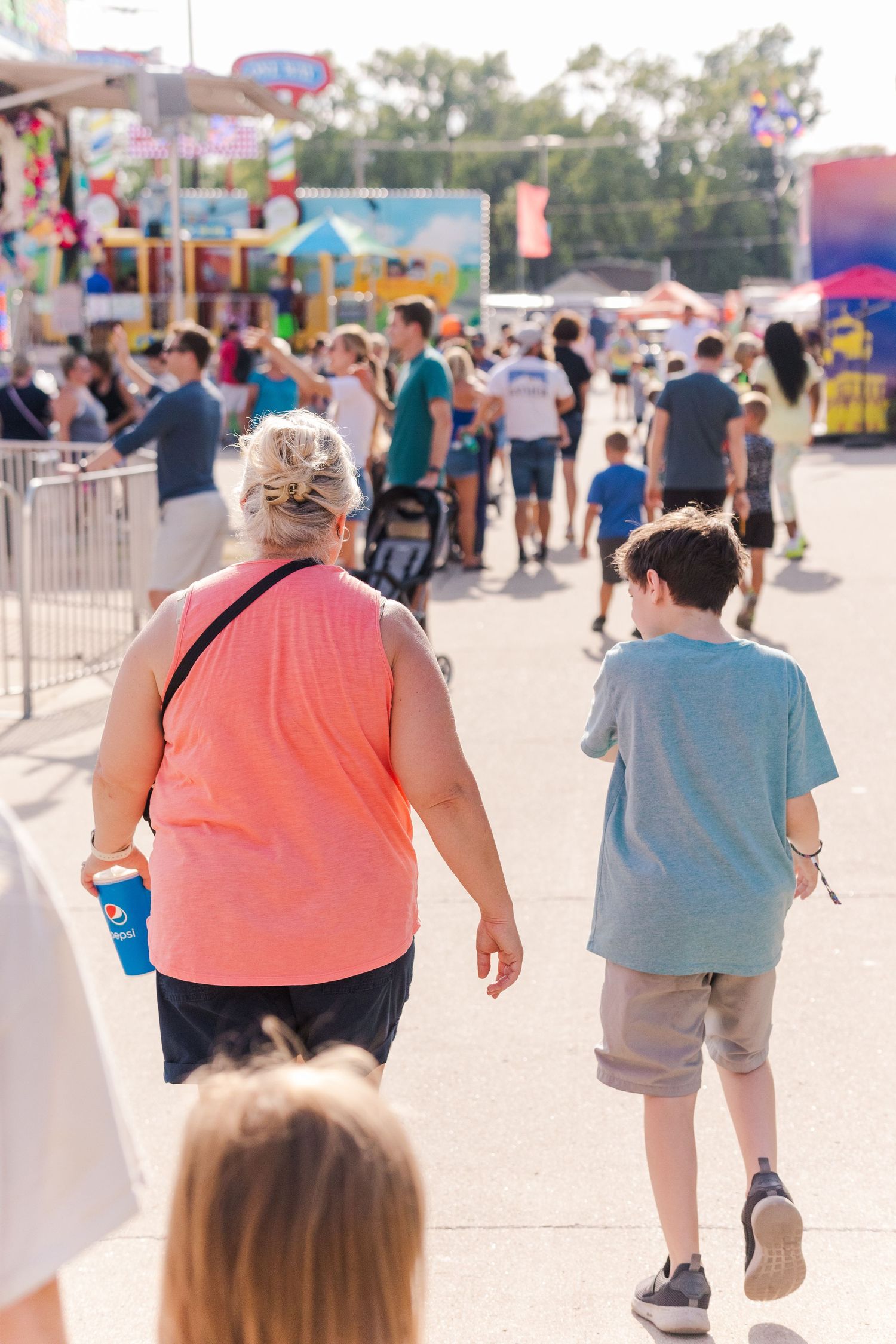 Visitors walking along a crowded carnival midway with game booths and attractions.