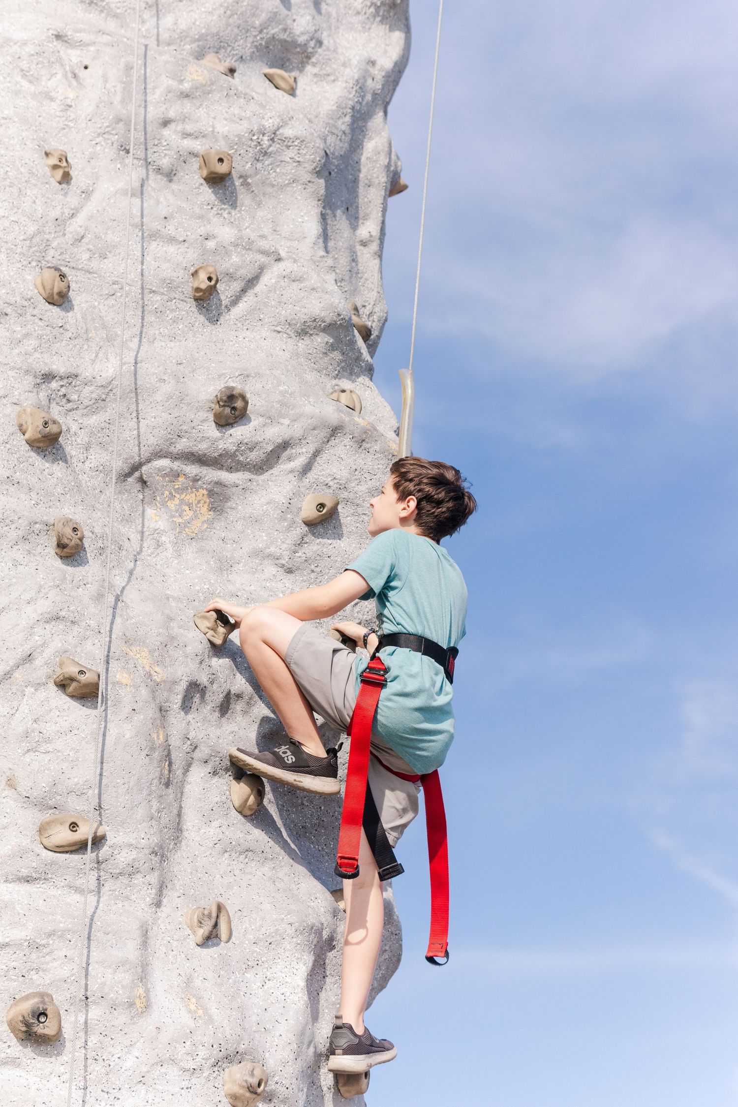 Person climbing a white outdoor rock climbing wall against blue sky.