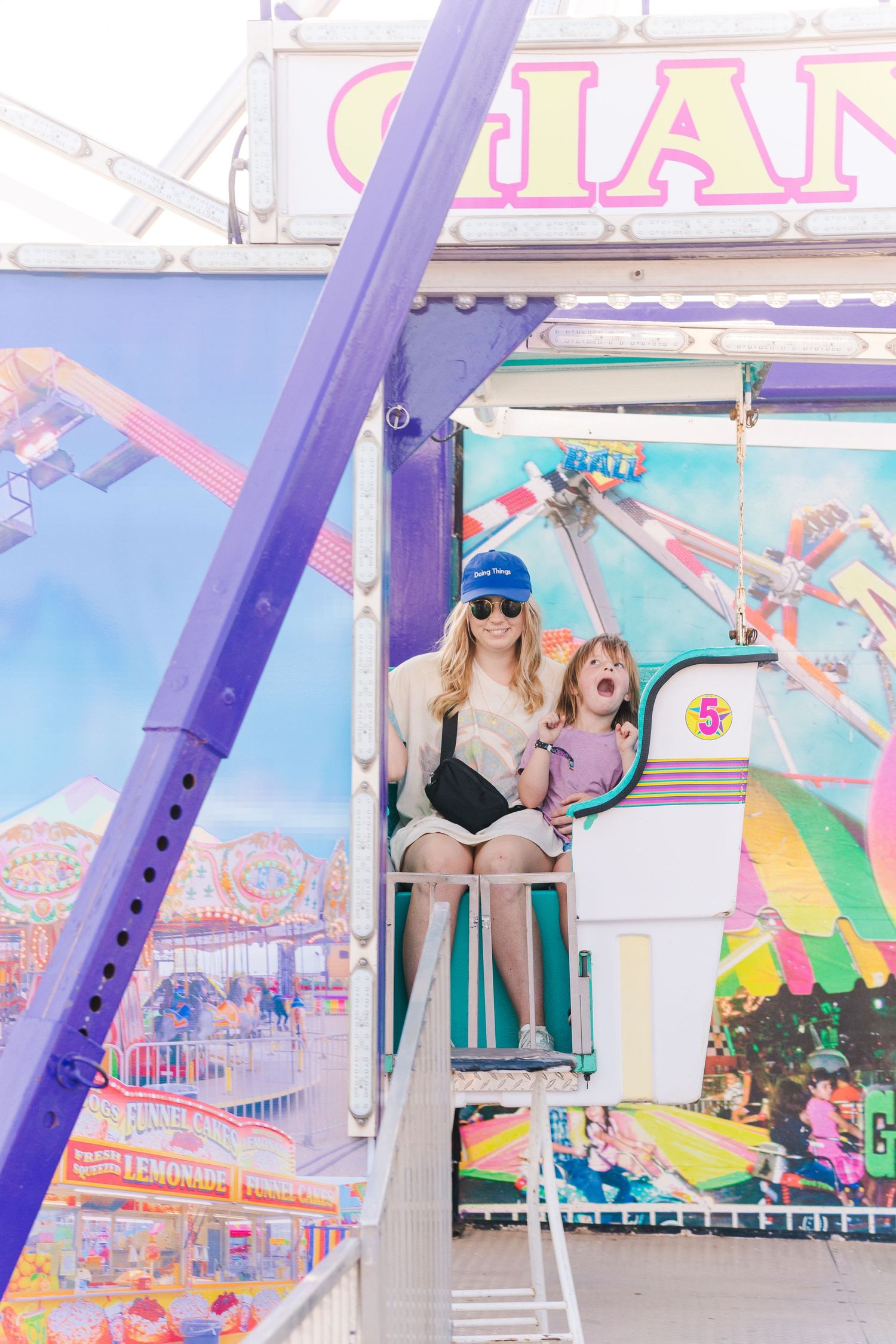 Carnival ride with purple and pink structural elements against bright blue sky.