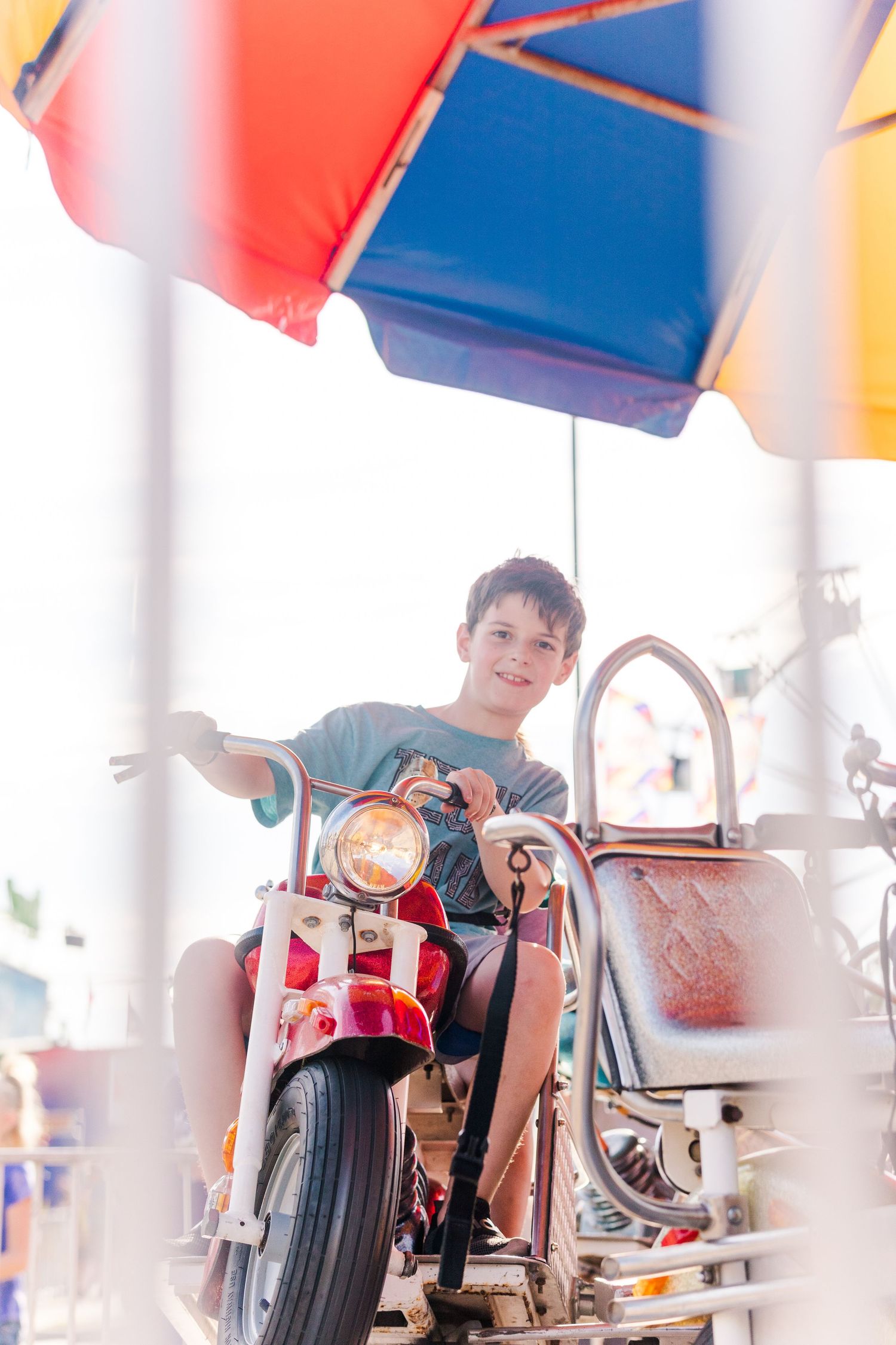 Vintage-style carnival motorcycle ride with red and chrome details under a striped canopy.