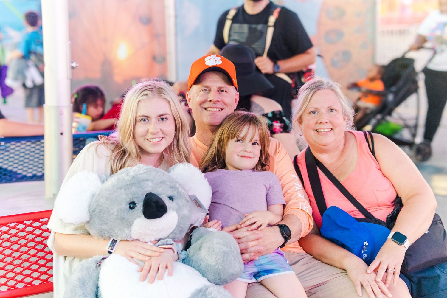 Family enjoying a day at the carnival with a large stuffed koala bear prize.