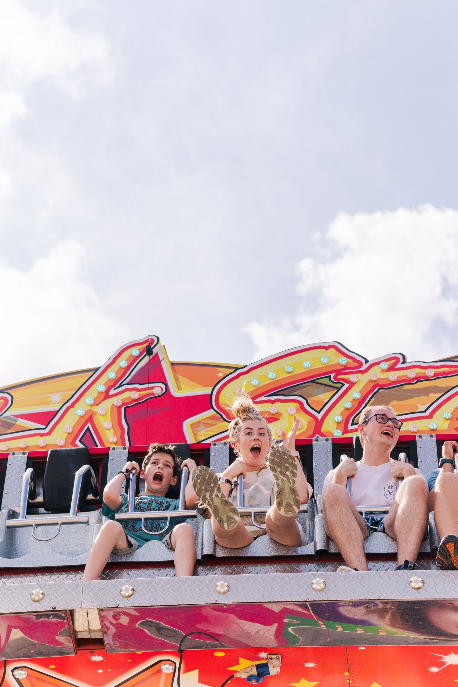 Excited riders screaming with joy on a carnival ride against cloudy sky.