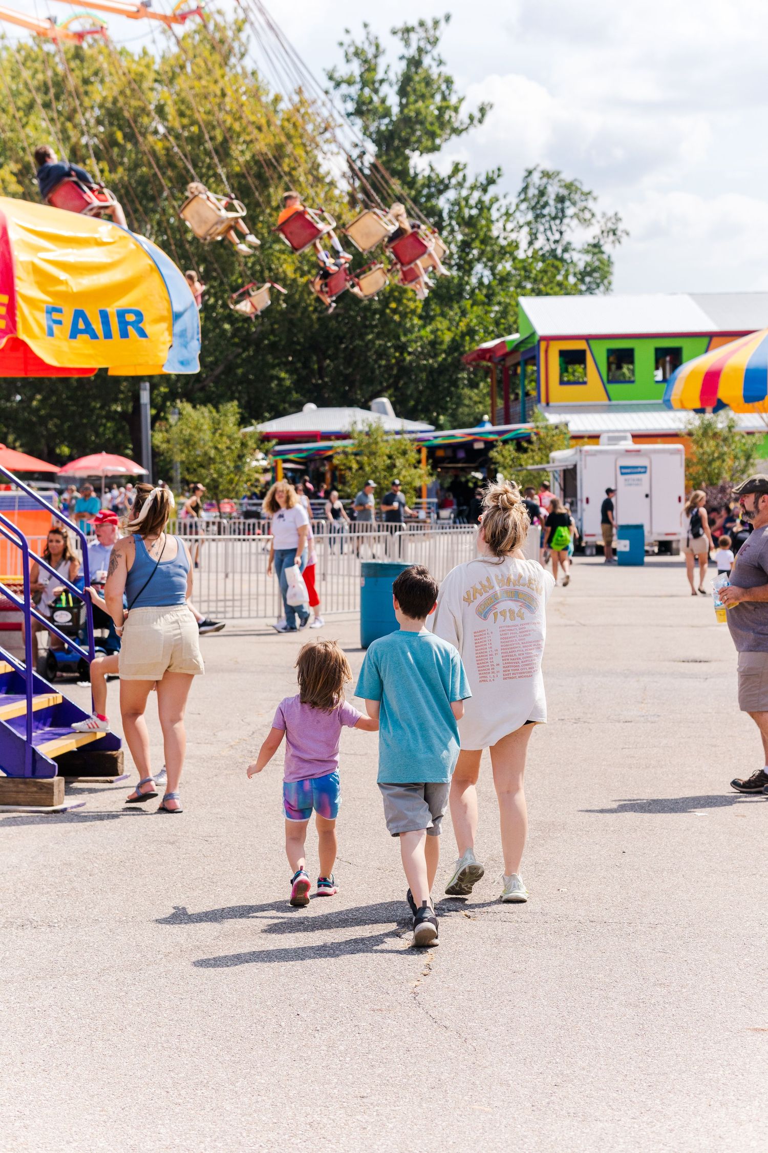 Families walking through a colorful fairground with rides and attractions.
