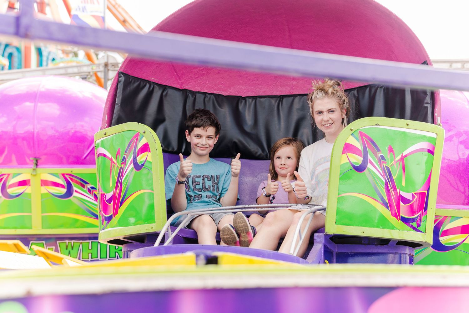 Riders enjoying a brightly colored carnival ride with pink and green decorative panels.