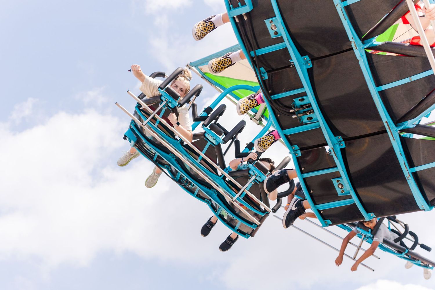 Thrill seekers enjoying an upside-down moment on a turquoise amusement park ride against blue sky.