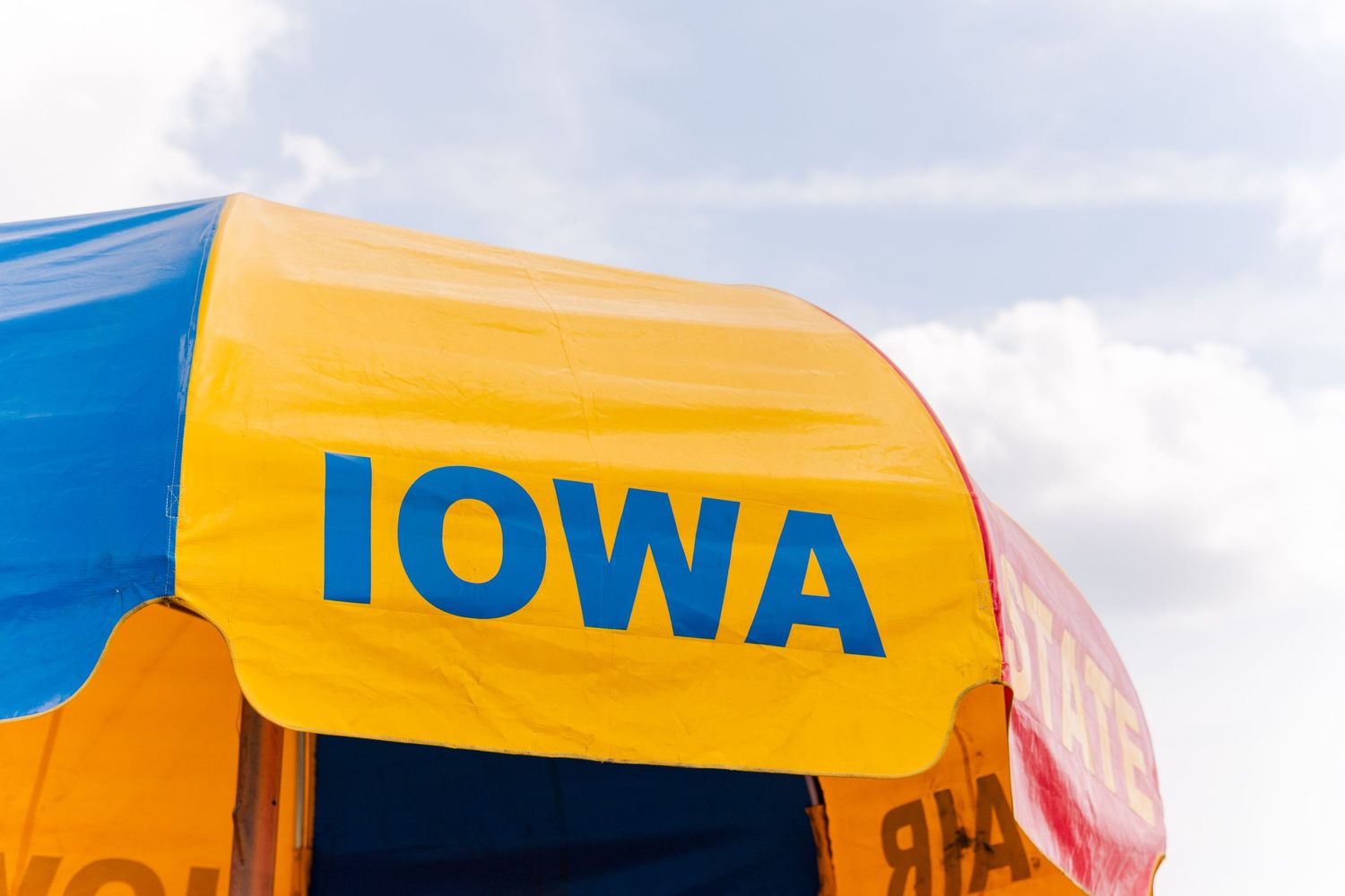 Yellow and blue Iowa state fair banner or tent top against cloudy sky.