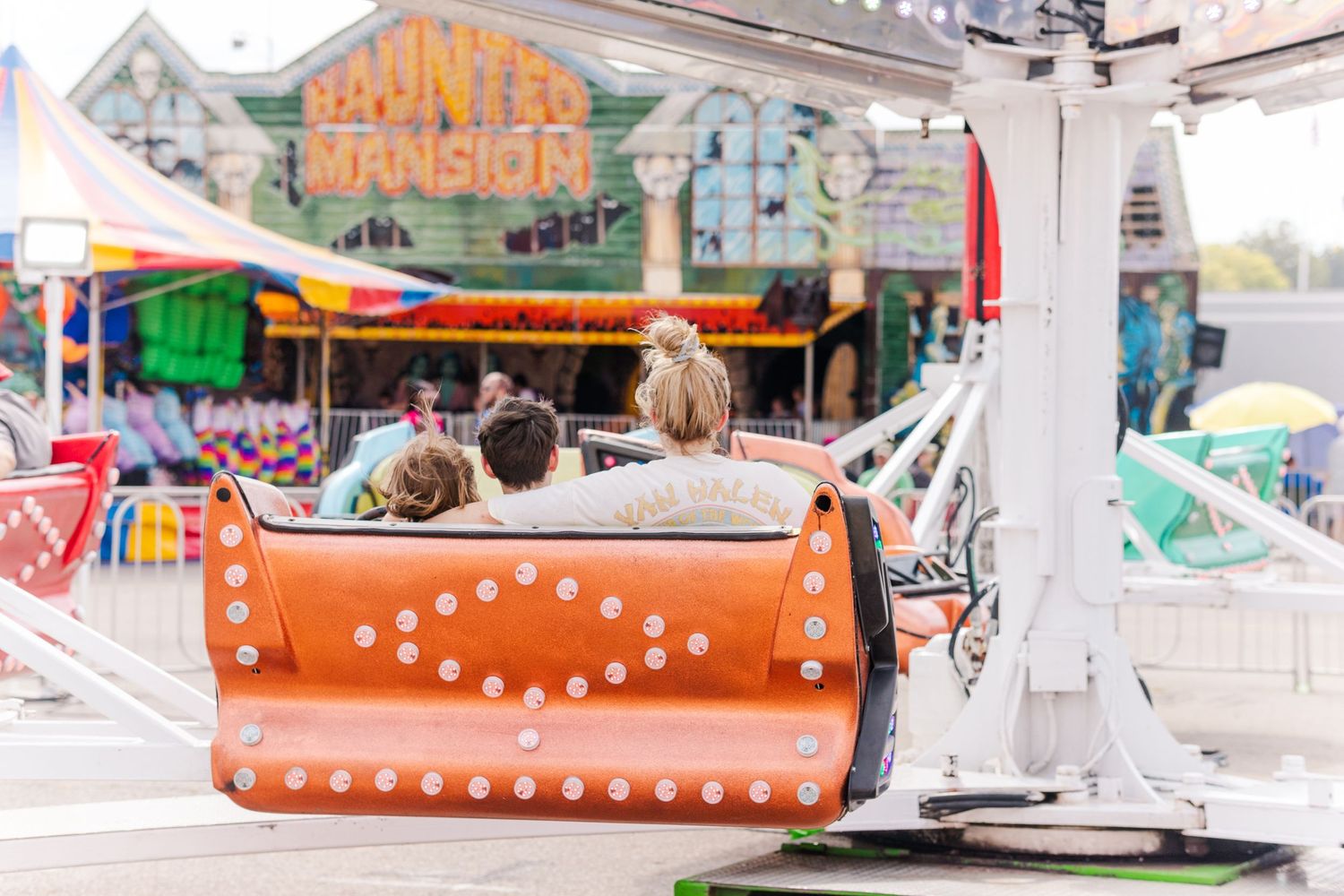 Orange carnival ride with decorative lights spinning against a bright summer sky.