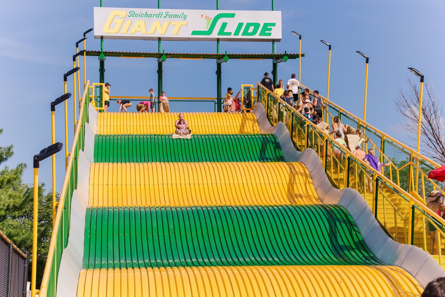 Large yellow and green slide attraction at a carnival with 'Slide' signage.