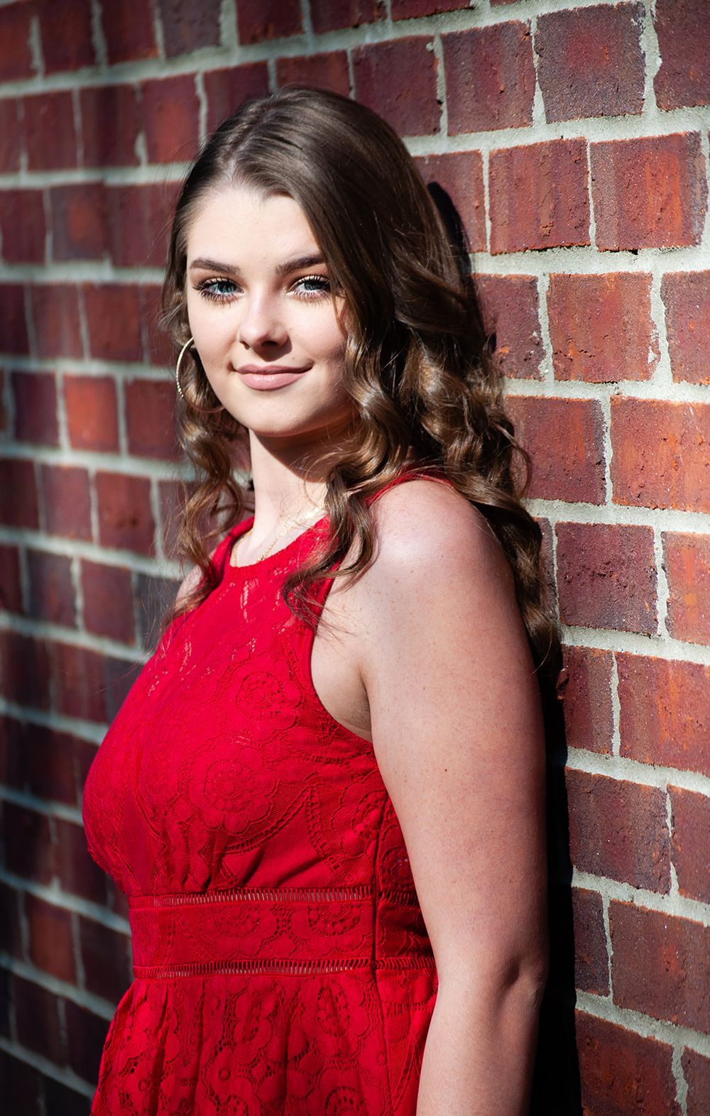 Red dress senior session leaning on a brick wall