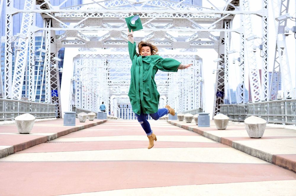 Celebrating graduation jump on city sky line bridge for senior photo session