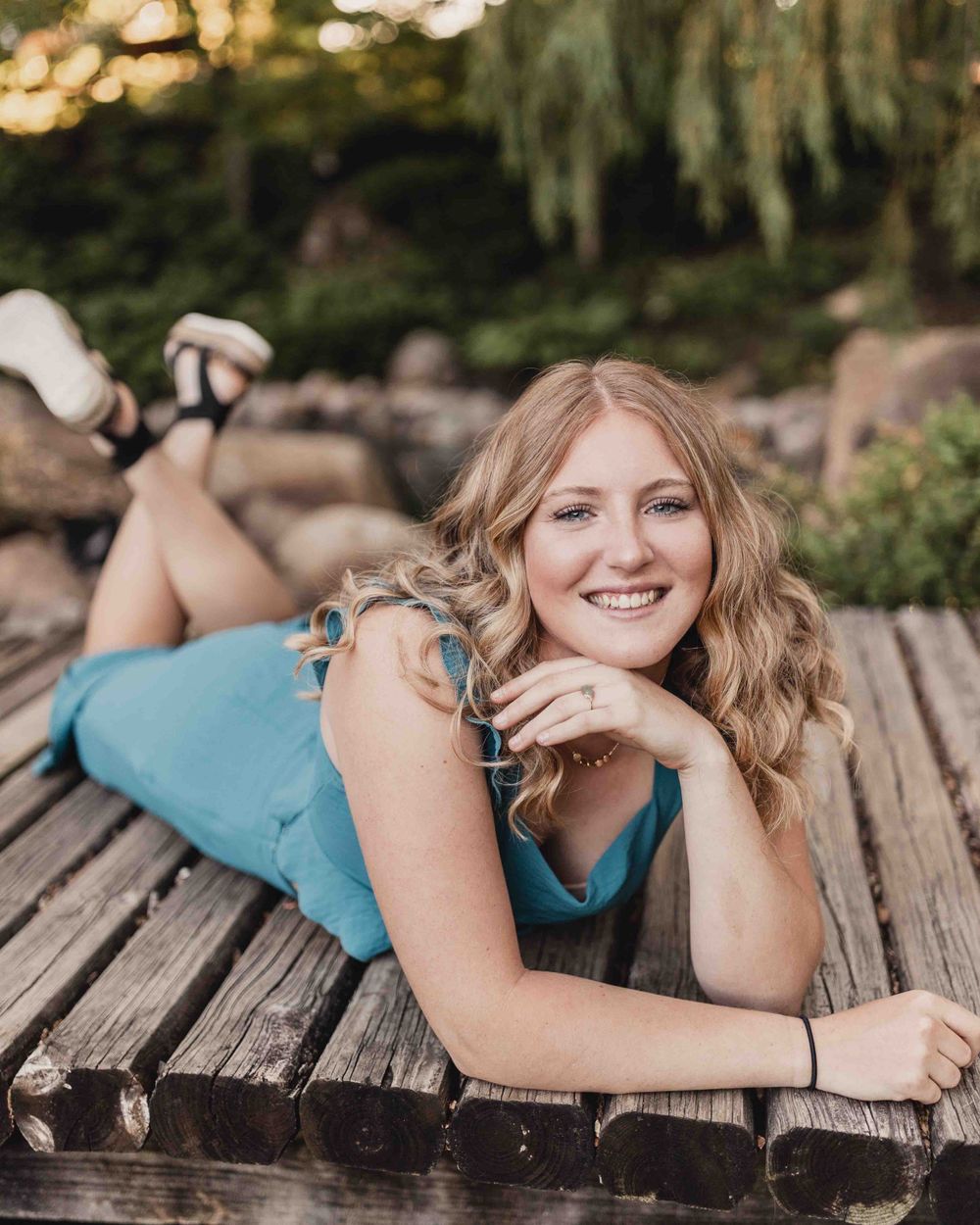 Senior portrait of female laying on bridge smiling outdoors at the Dubuque Iowa Arboretum and Botanical Gardens